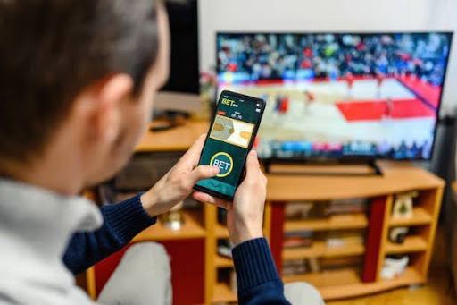 A young adult watching basketball while using mobile betting apps.